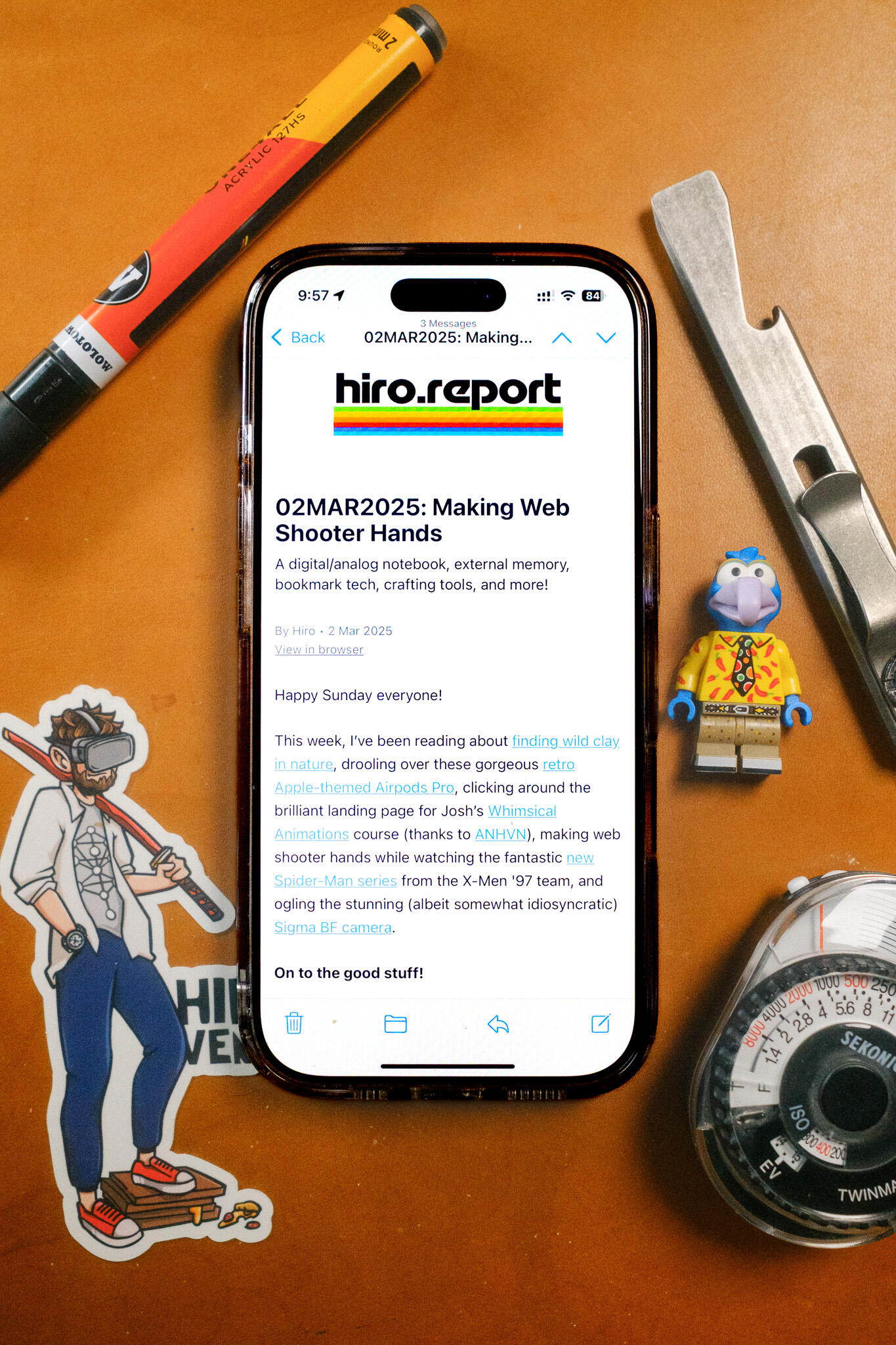 Photo of an iPhone displaying a recent issue of the Hiro Report newsletter, laying on a blue background surrounded by gear.